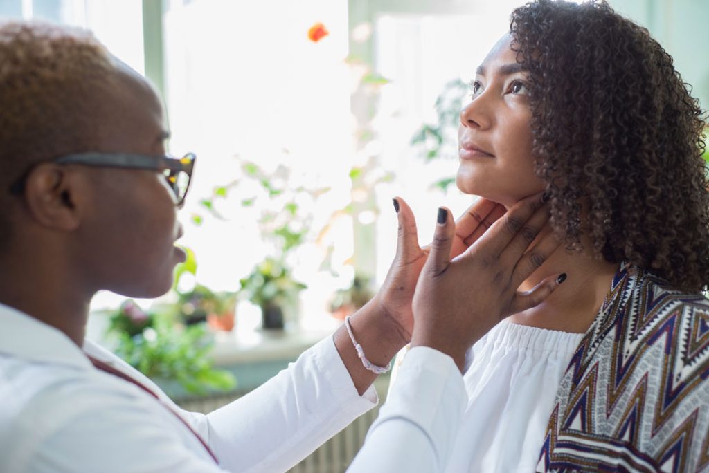 Black woman having thyroid checked by doctor