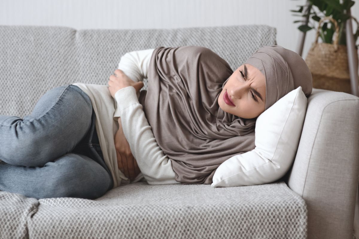 Muslim woman lying on couch with stomach pain