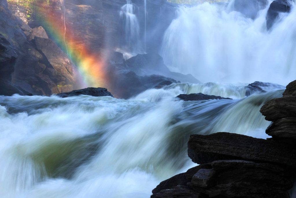 angry river flowing fast with a rainbow in background