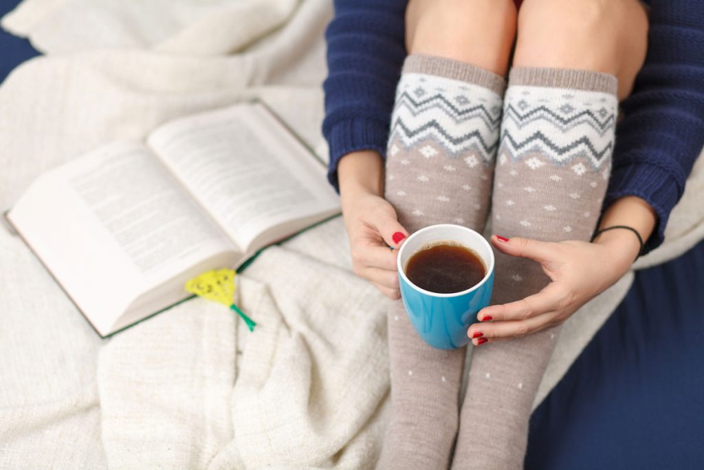 cold woman warming up with hot coffee and socks