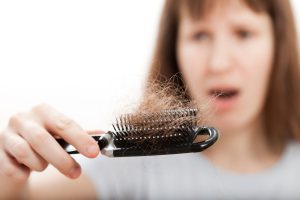 woman looking at hair loss on brush