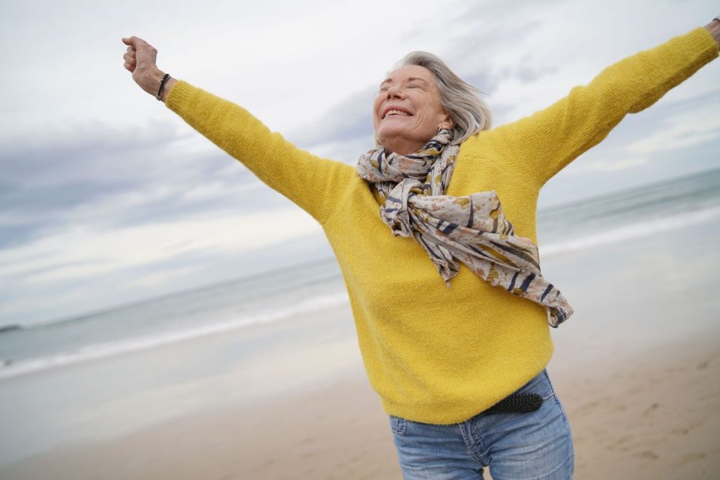 Aging woman with arms outstretched on beach feeling good about herself