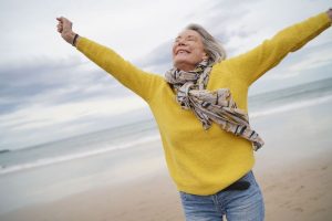 Aging woman with arms outstretched on beach feeling good about herself